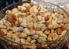 A close-up view of a glass bowl filled with various mixed nuts, including almonds, cashews, and pistachios.